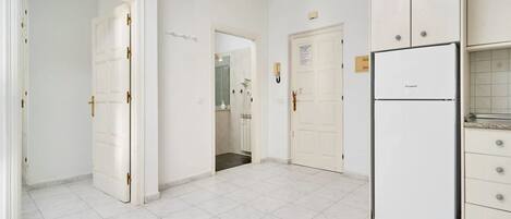 A kitchen with white cabinets, a white refrigerator, and a tiled floor.