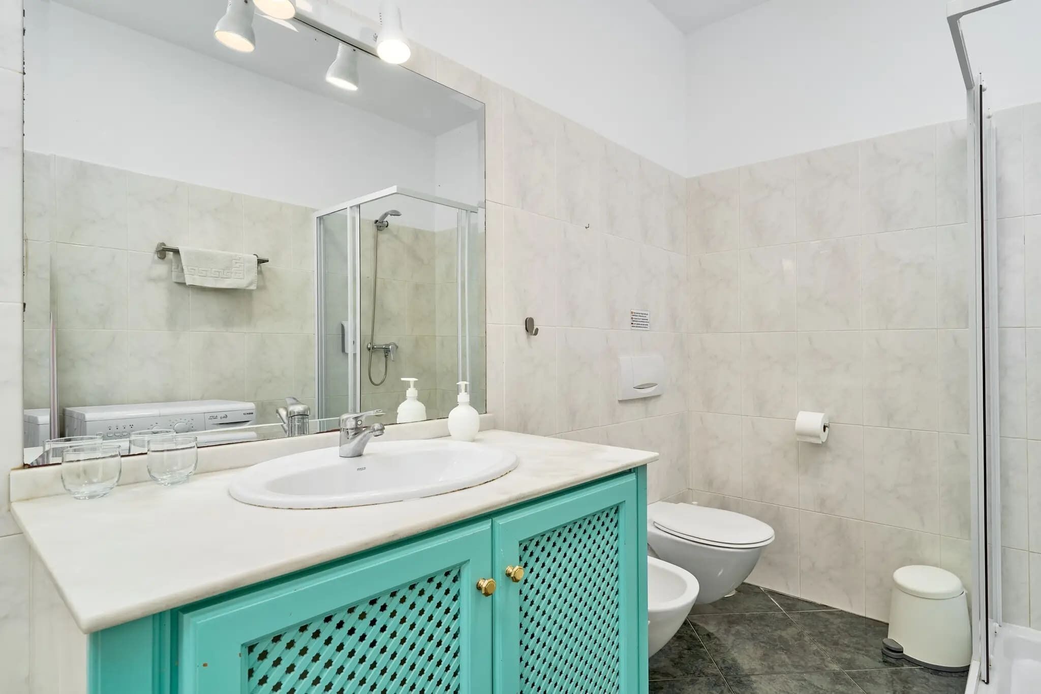 Un baño con lavamanos blanco, espejo, inodoro y zona de ducha.