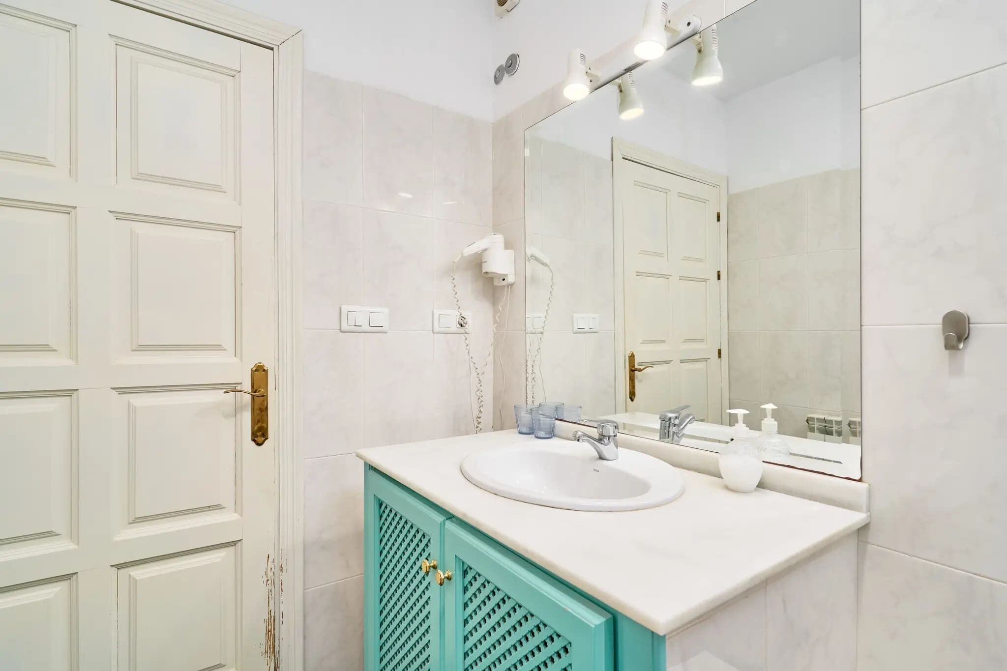 Un baño con un lavamanos blanco, un espejo, un secador de pelo y un armario color turquesa.