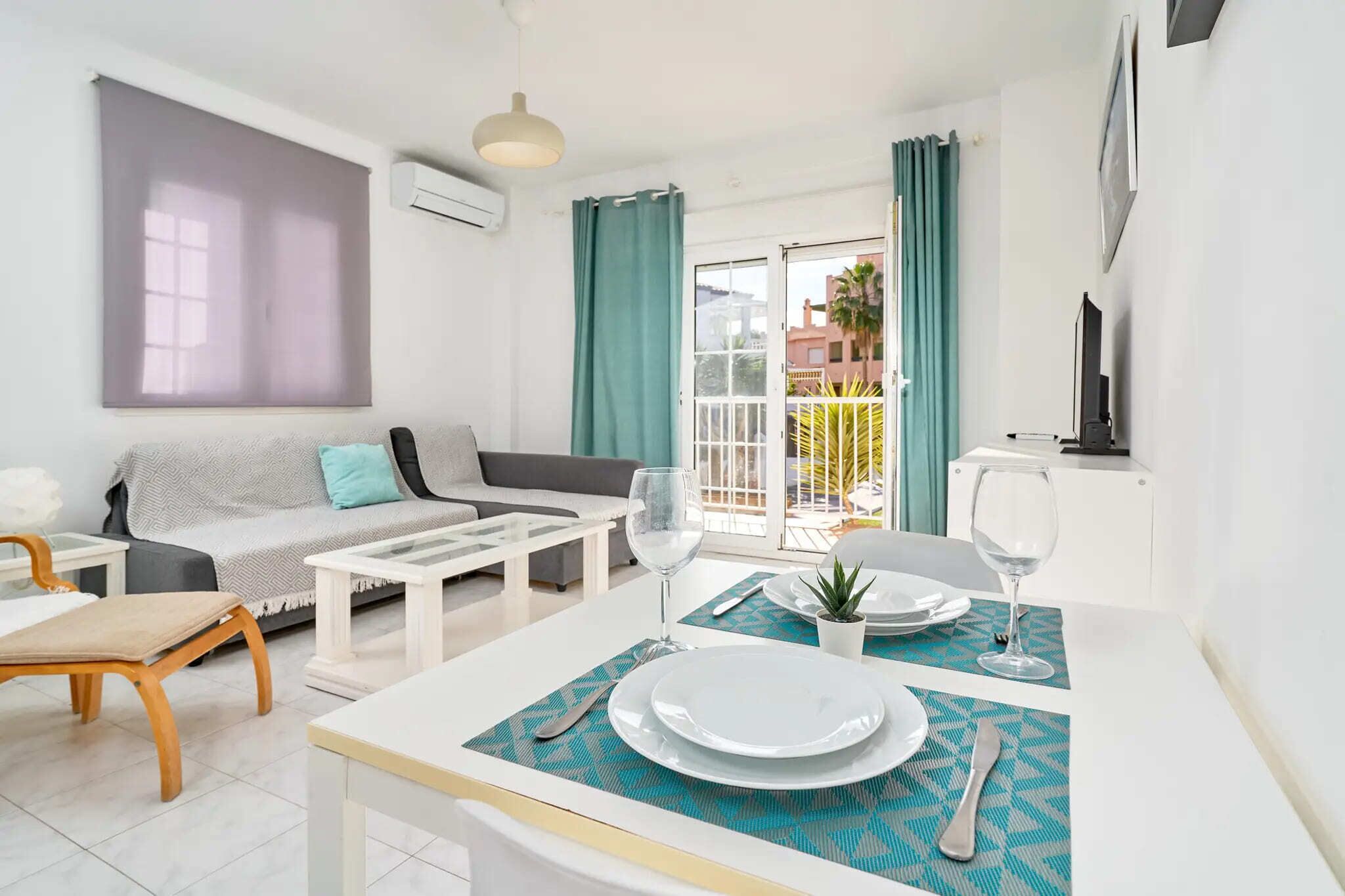 A modern living room with a sofa, coffee table, dining table set for two, and a balcony with curtains.