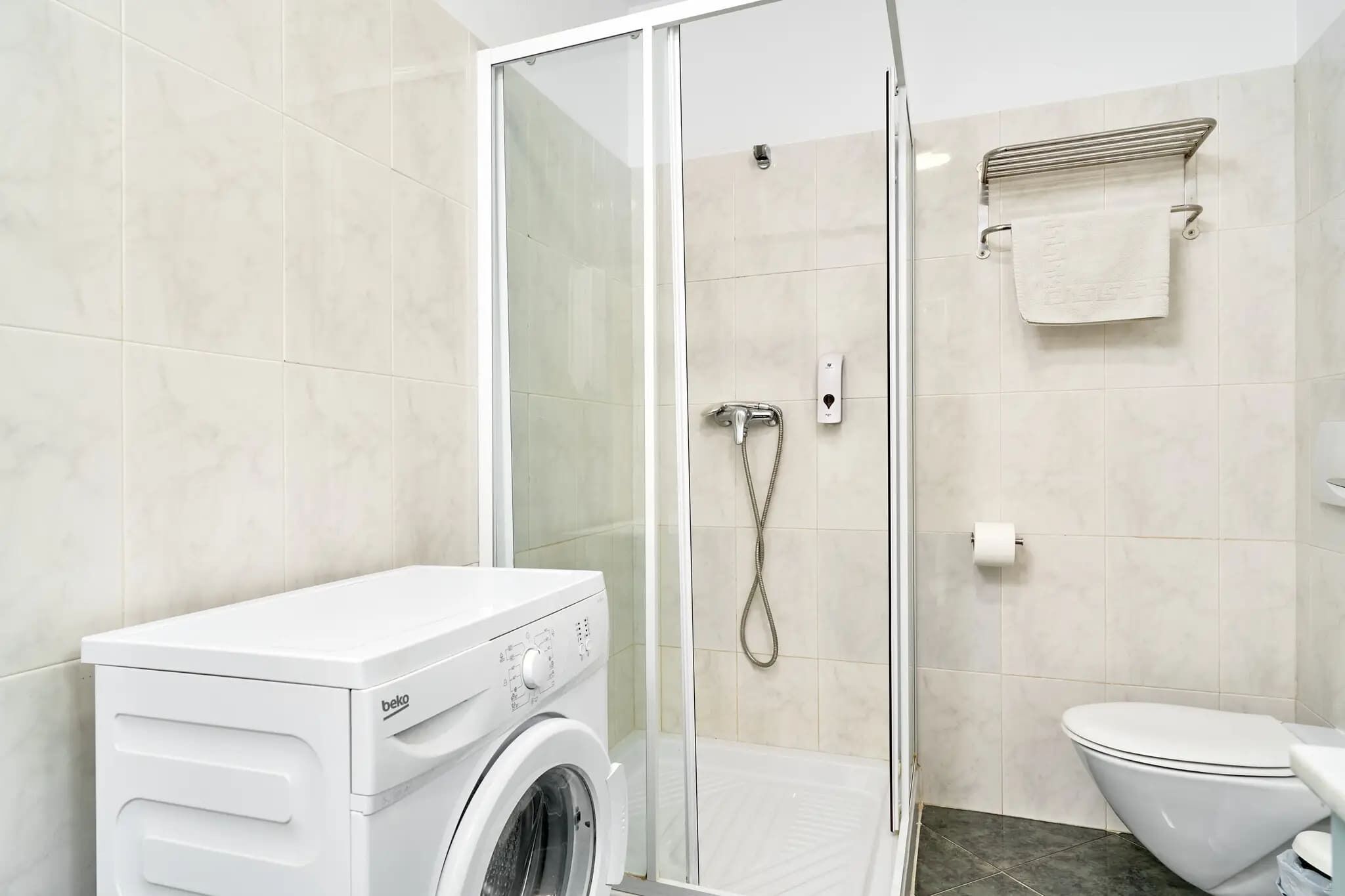 A modern bathroom with a glass-enclosed shower, a white washing machine, and a toilet.