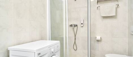 A modern bathroom with a glass-enclosed shower, a white washing machine, and a toilet.