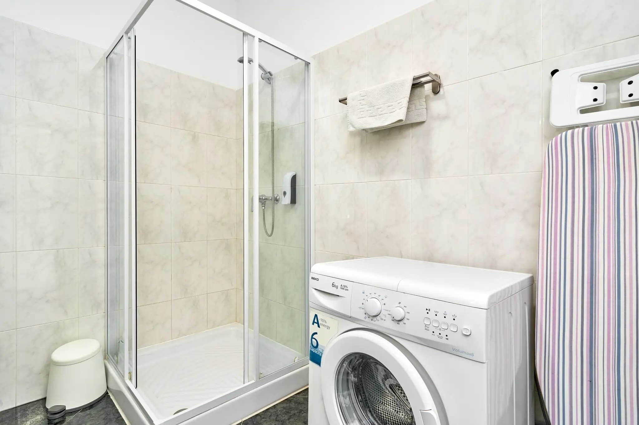 Baño con cabina de ducha de vidrio, lavadora y toallero a rayas.