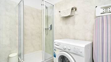 Baño con cabina de ducha de vidrio, lavadora y toallero a rayas.