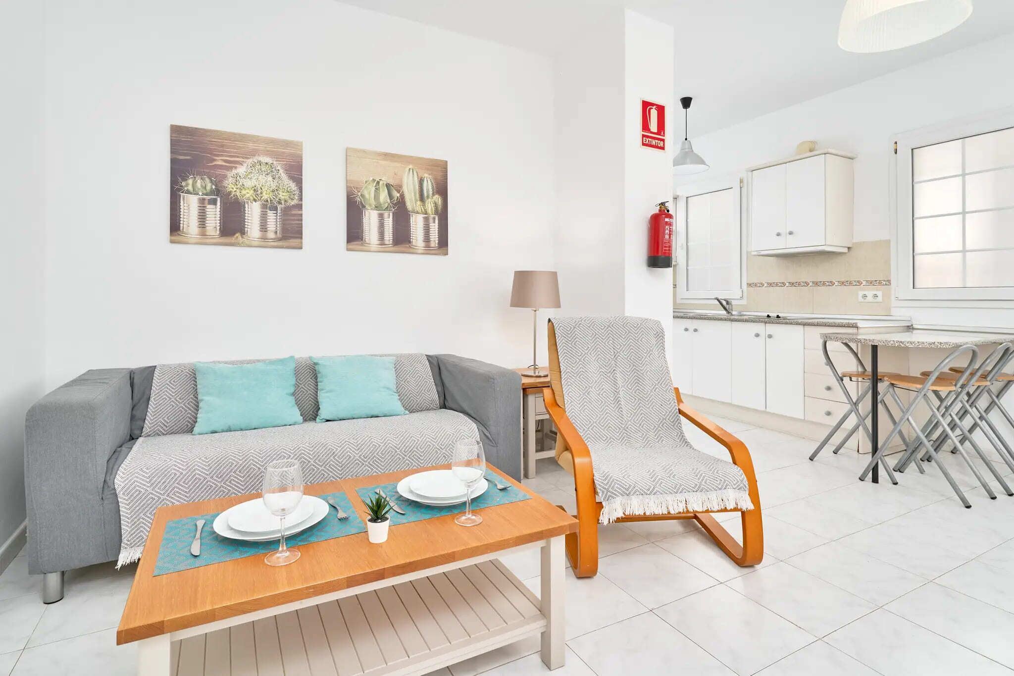 A modern living room with a sofa, armchair, dining table, and kitchen area.