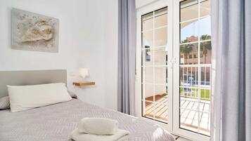 A hotel room with a bed, a painting on the wall, a window with curtains, and a view of the outside.