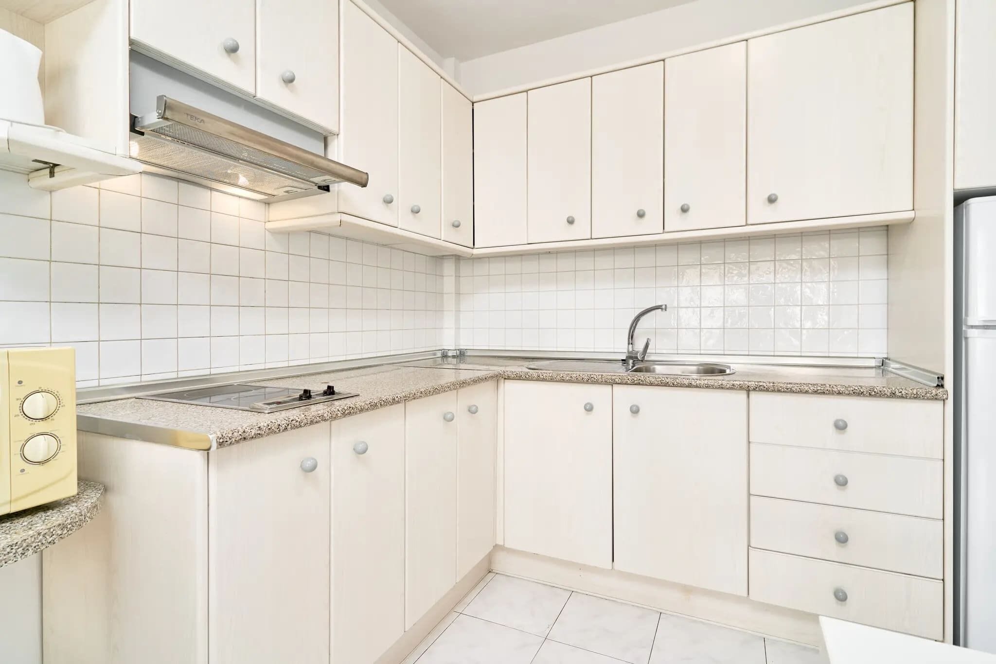 A kitchen with white cabinets, a stainless steel sink, and a built-in range hood.