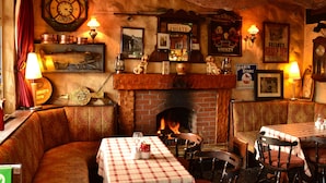 Un pub acogedor con chimenea de ladrillo, manteles a cuadros y decoración vintage, incluyendo un reloj de Titanic y un cartel de Whisky Robin Starc.