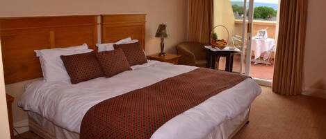 A hotel room with a large bed, a nightstand, a lamp, a chair, and a view of the outdoors.