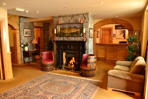 A cozy lobby with a stone fireplace, comfortable seating, and a reception desk. - Fairhill House Hotel (Clonbur)