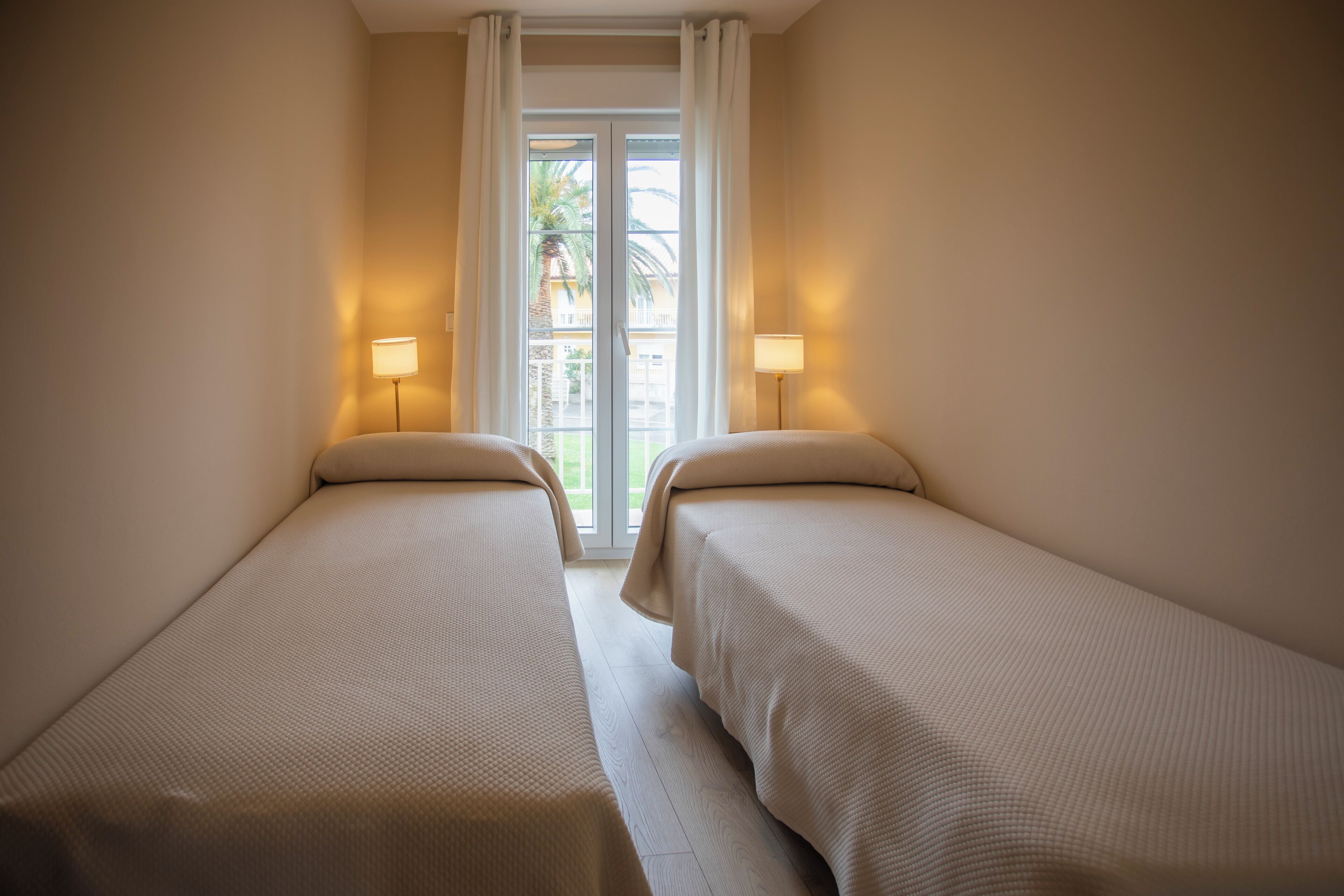 A room with two beds, a window with curtains, and two bedside lamps.