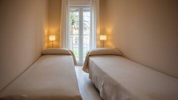 Una habitación con dos camas, una ventana con cortinas y dos lámparas de noche.