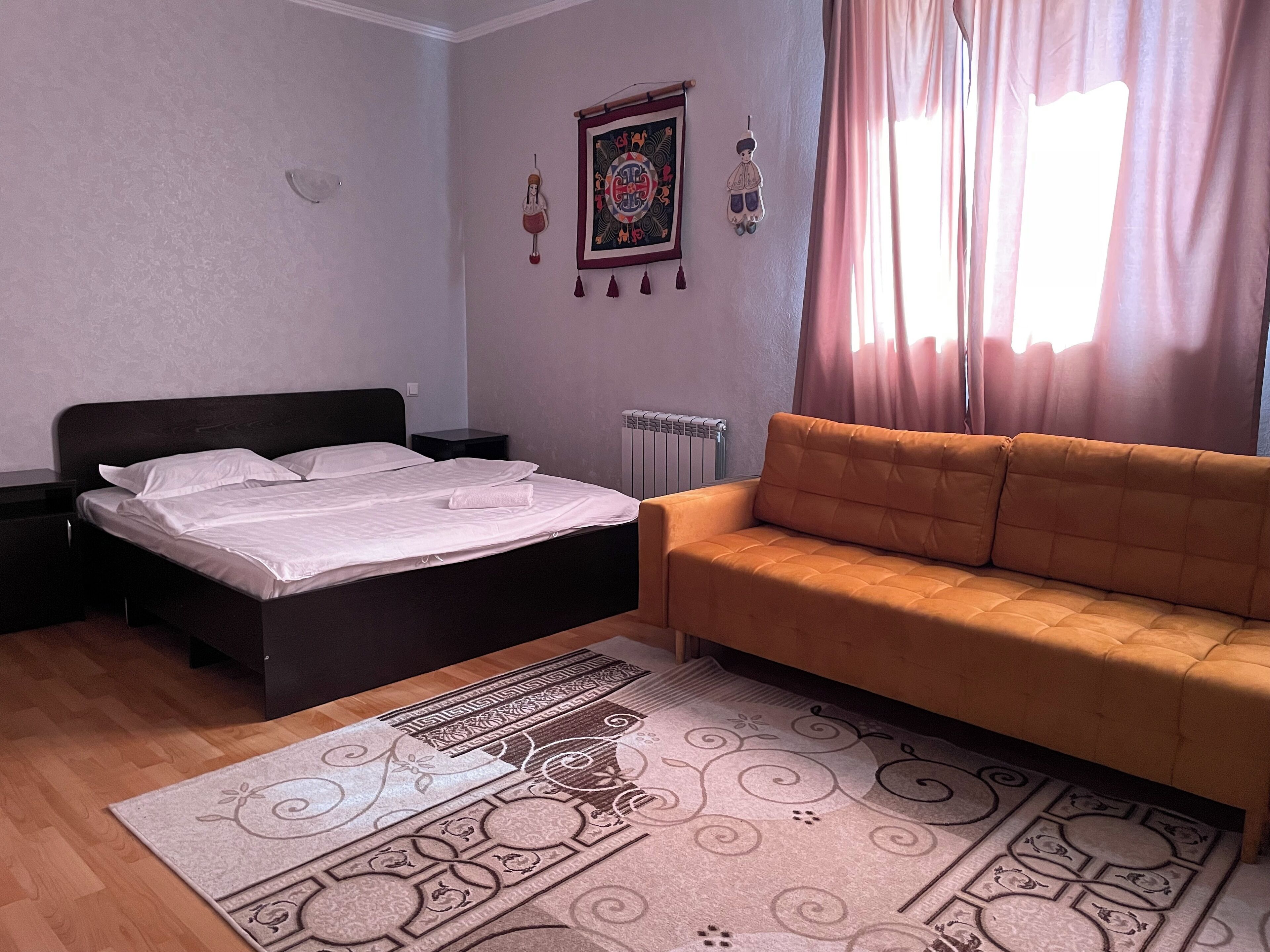 A bedroom with a bed, a sofa, a radiator, and a decorative rug.