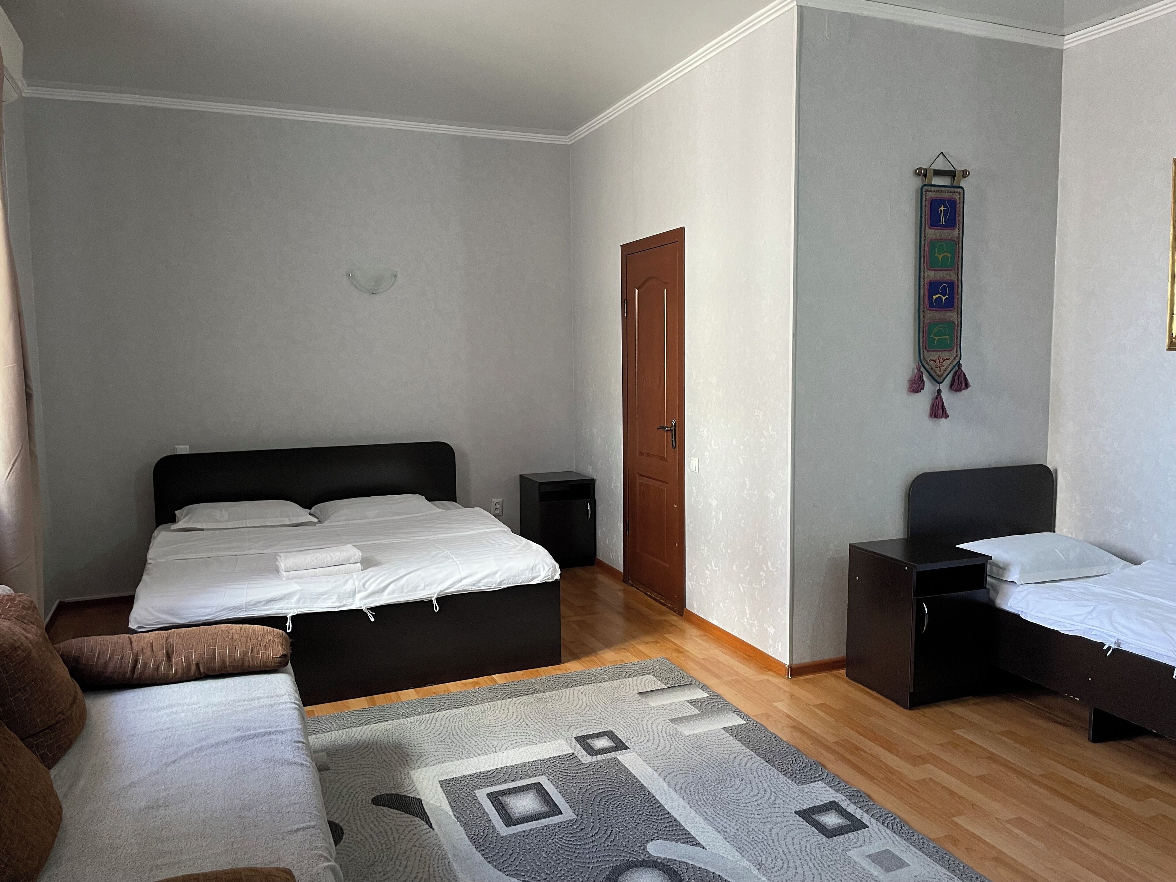 A bedroom with a bed, a bedside table, a chair, a wardrobe, a rug, and a wall decoration.