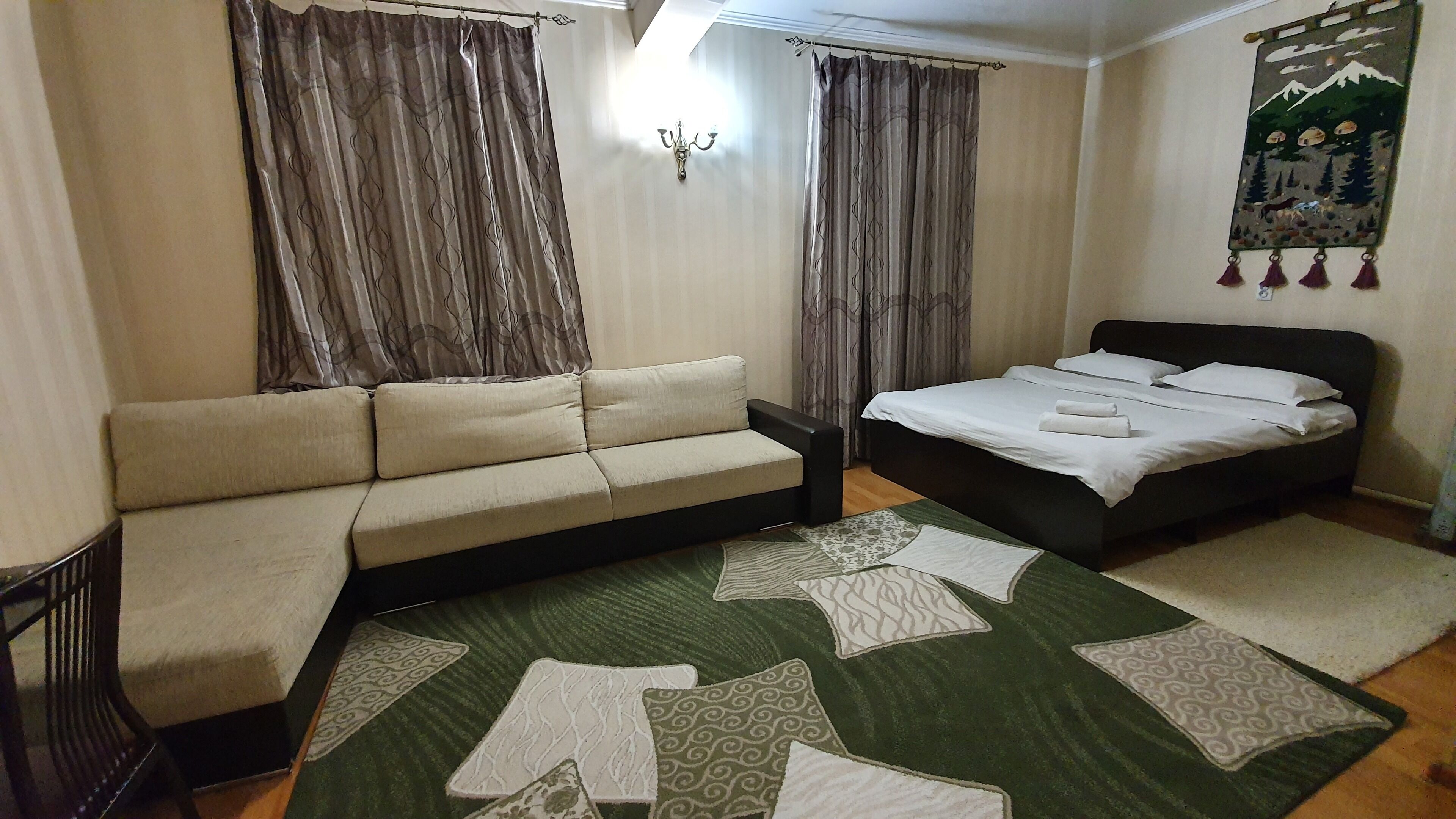 Un dormitorio con sofá, cama, alfombra estampada y cortinas.