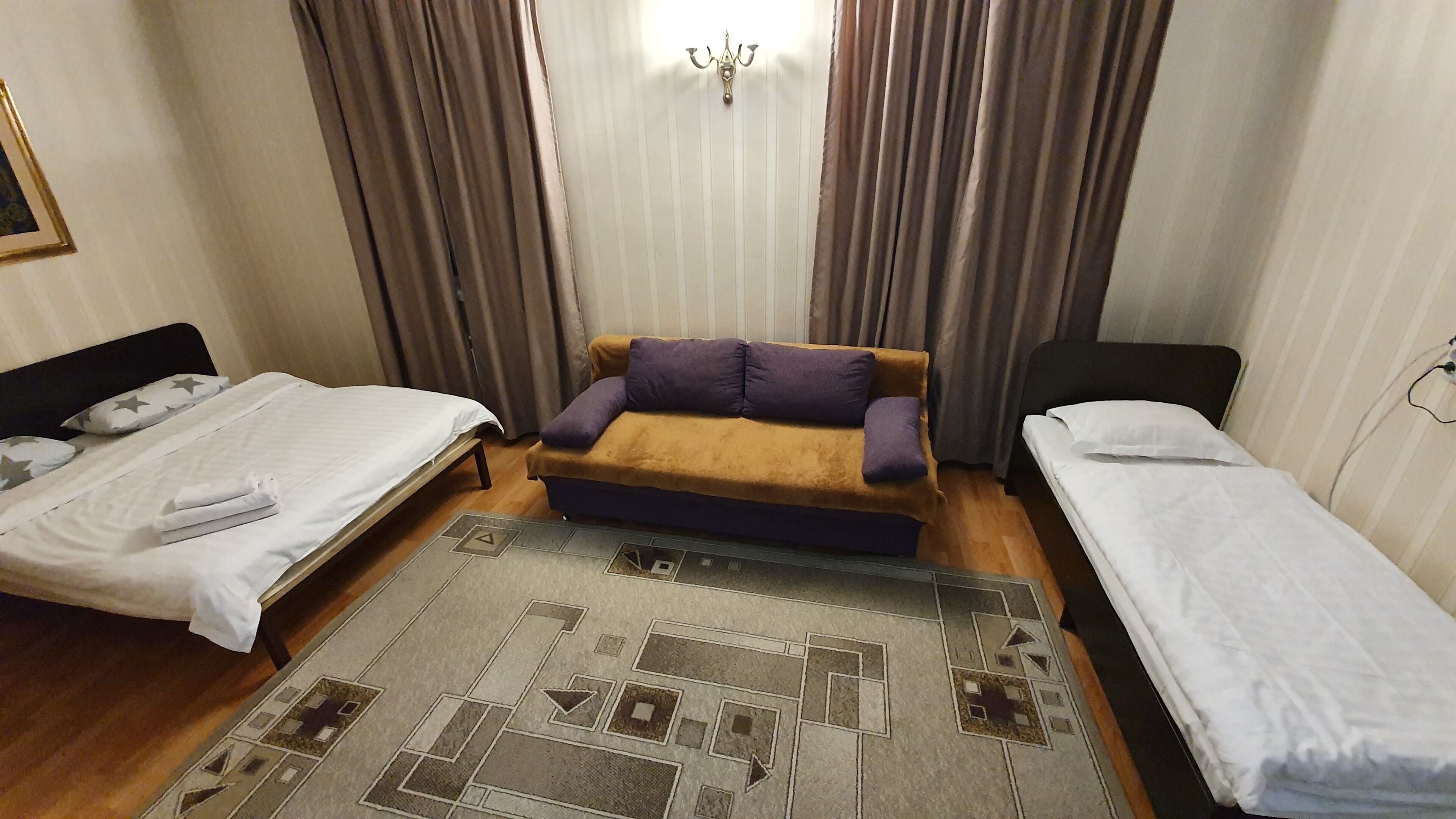 A hotel room with two single beds, a sofa, a rug, and curtains.