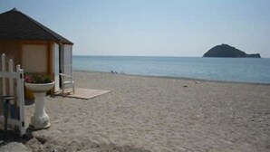 Una playa con una cabaña de madera pequeña, una silla blanca y una planta en maceta.