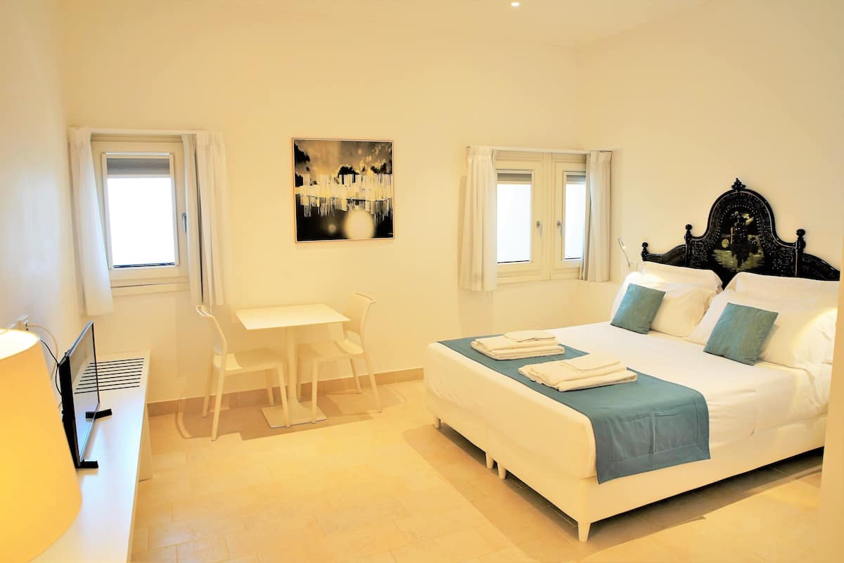 A bedroom with a bed, a desk, and two windows.