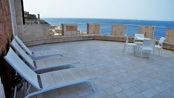 A terrace with white chairs and tables, overlooking the sea.