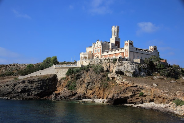 Un edificio con aspecto de castillo, con una torre, ubicado en un acantilado rocoso junto al mar.
