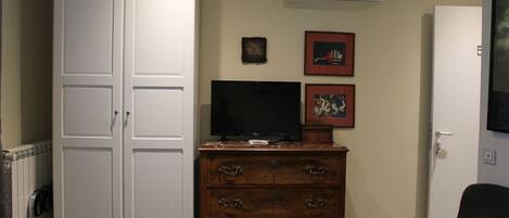 A room with a white wardrobe, a wooden dresser, a television, and a door.