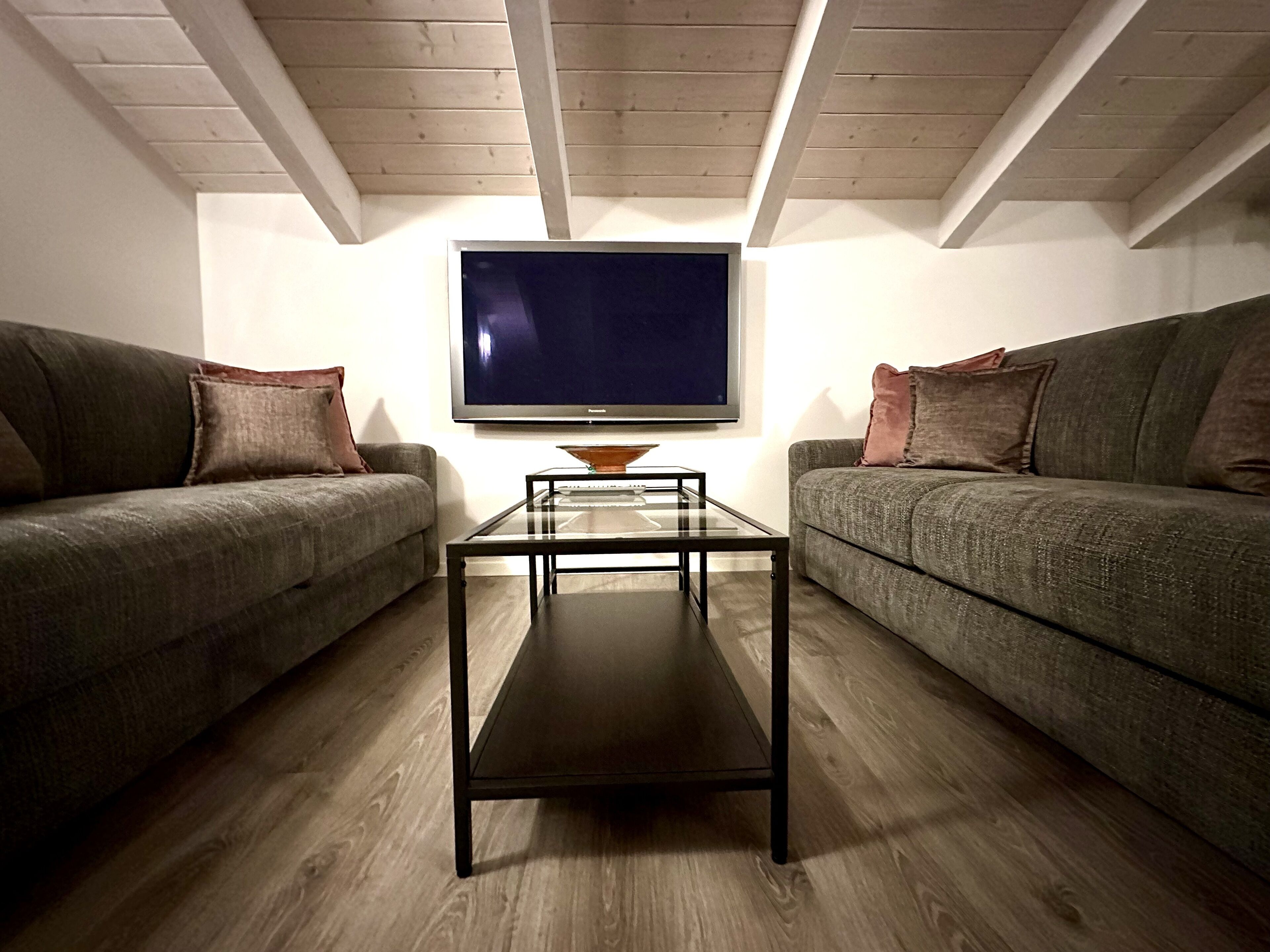 Una sala de estar con dos sofás grises, una mesa de centro de vidrio y un televisor de pantalla plana montado en la pared.