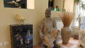 A room with a checkered floor, a statue of a seated figure, a cabinet with artwork, and a vase with plants. - Villa Abbamer (Grottaferrata)