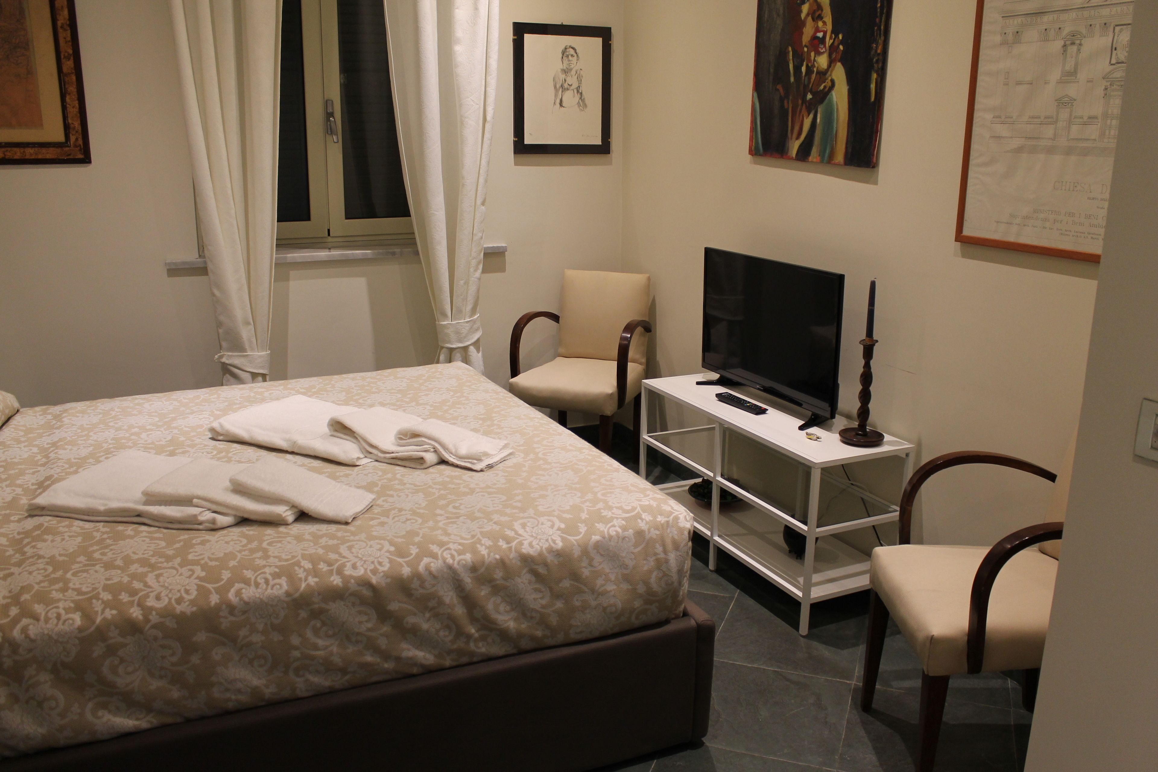 A bedroom with a bed, a TV, a chair, and a desk.