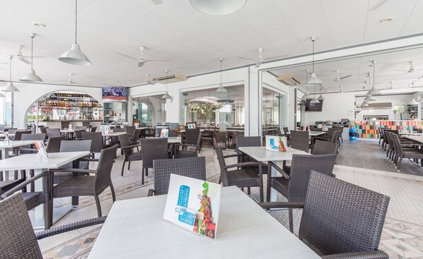 Un restaurante moderno con mesas y sillas blancas, una zona de bar y una pantalla de televisión.