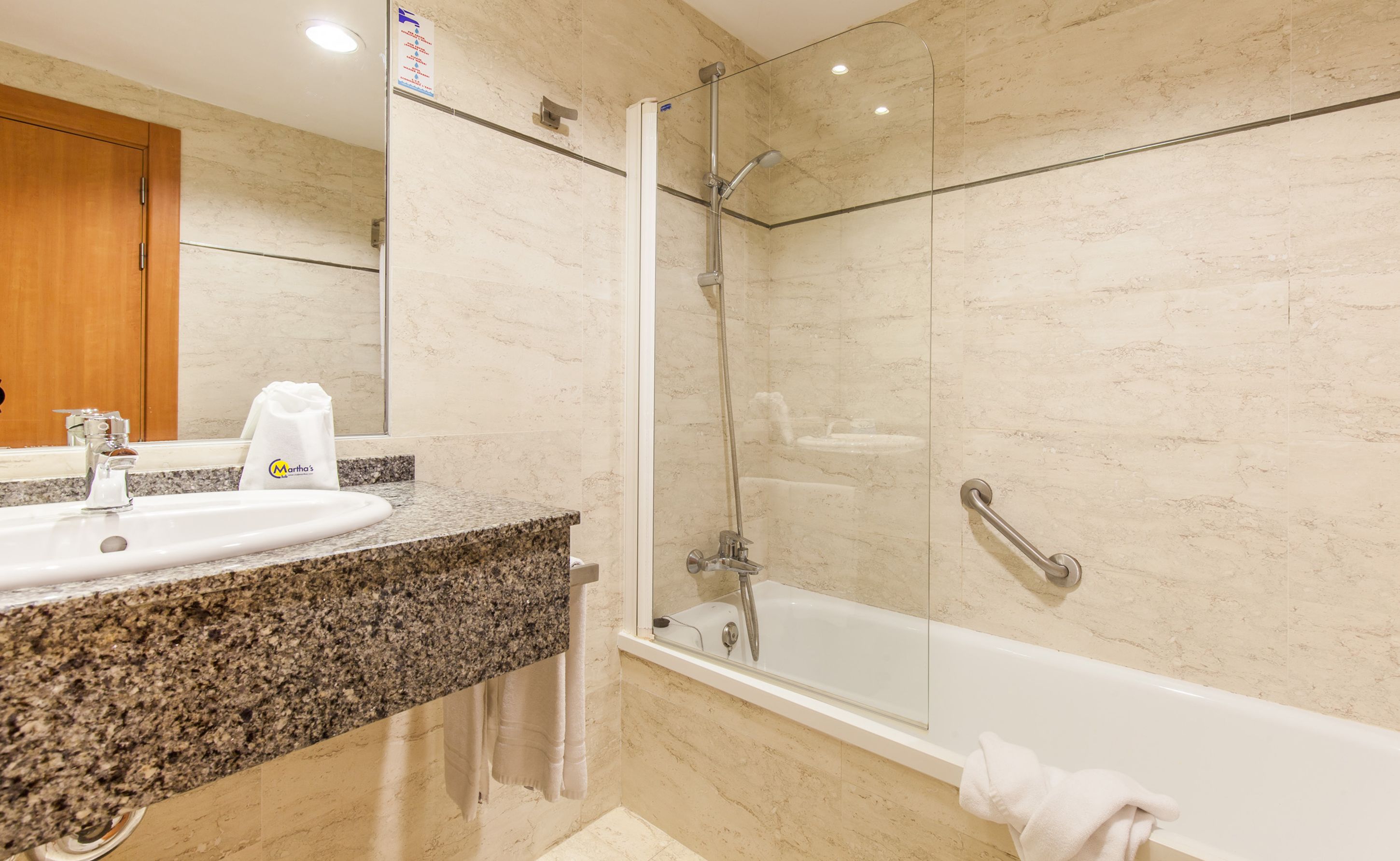 Un baño con lavamanos de encimera de granito, ducha con cerramiento de vidrio y bañera blanca.