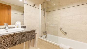 Un baño con lavamanos de encimera de granito, ducha con cerramiento de vidrio y bañera blanca.