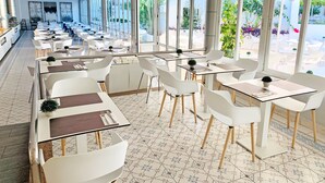Un restaurant moderne avec des chaises et des tables blanches, de grandes fenêtres et un sol carrelé.