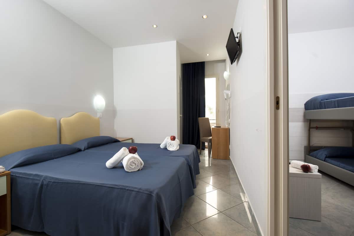 Quarto de hotel com duas camas, uma mesa, uma cadeira e uma televisão fixada na parede.
