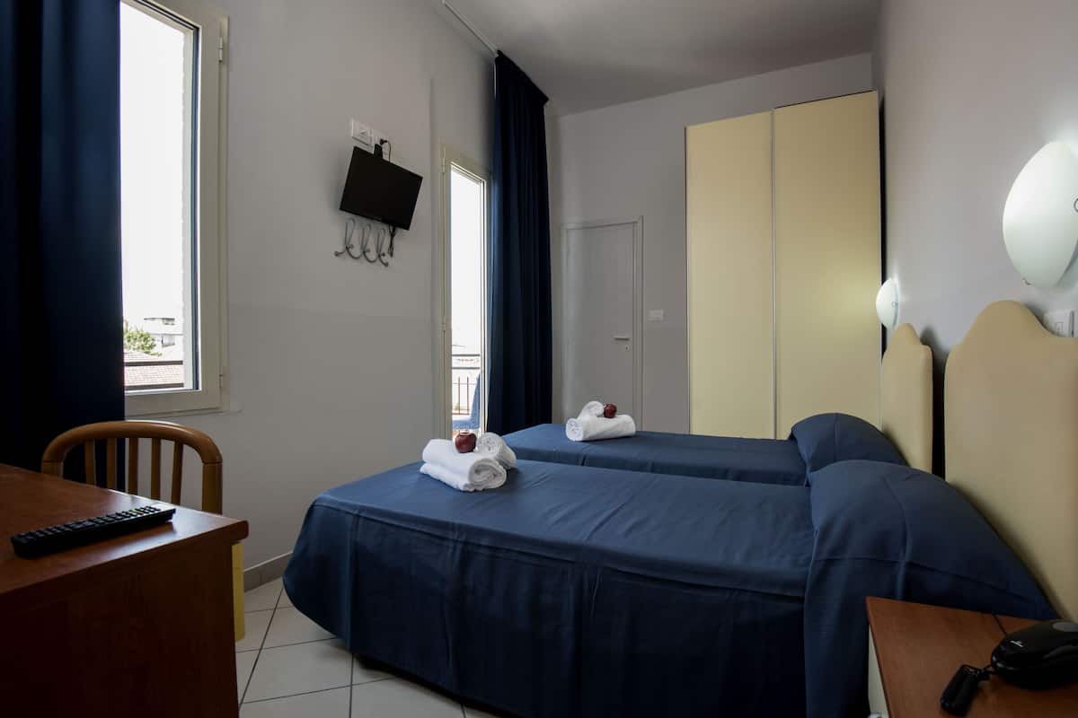 Quarto de hotel com duas camas, uma escrivaninha, uma cadeira, uma televisão e um guarda-roupa.