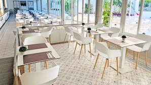 Un ristorante moderno con sedie e tavoli bianchi, ampie finestre e un pavimento piastrellato.