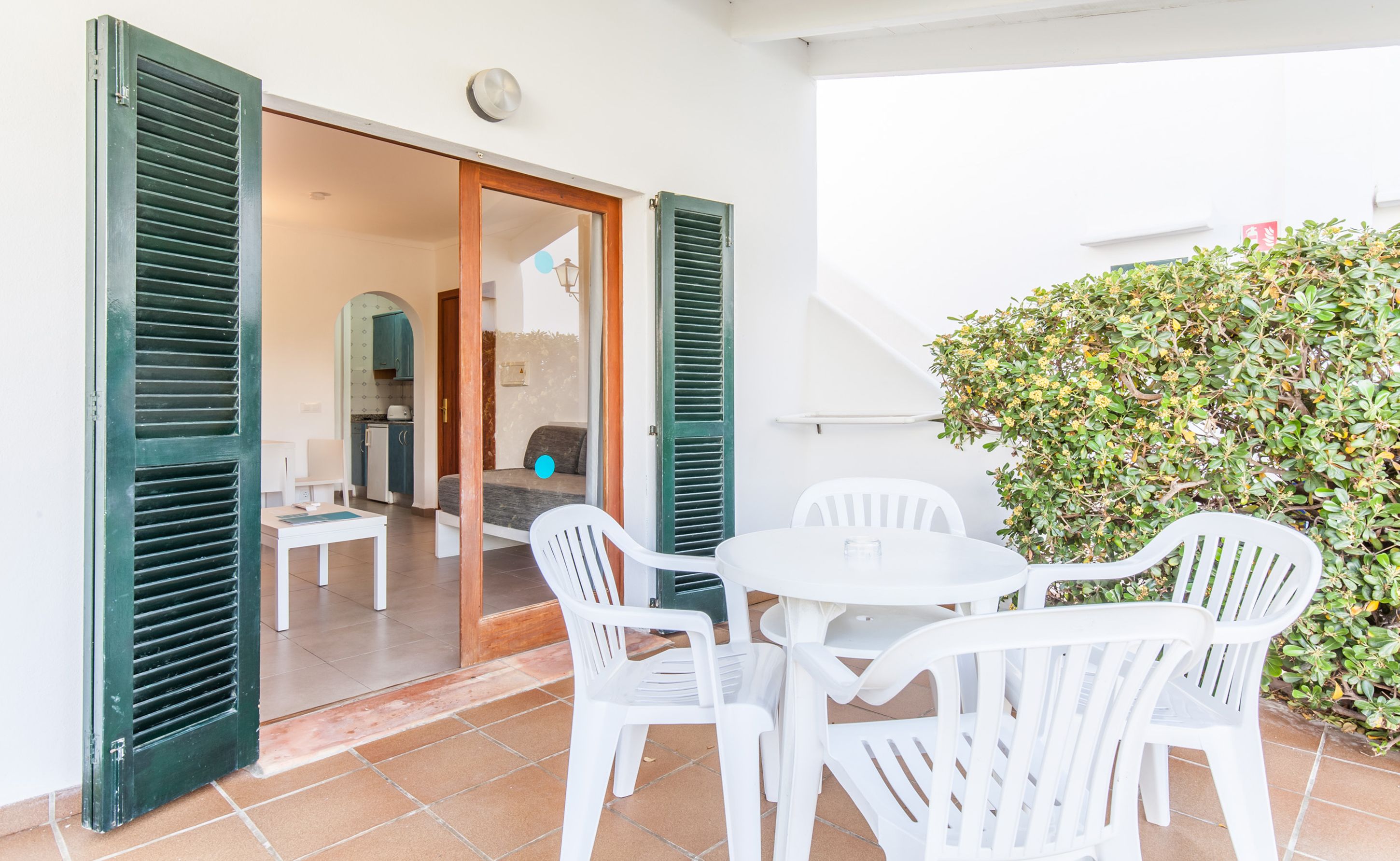 A patio with a table and chairs, a sliding glass door, and a view into a kitchen area.