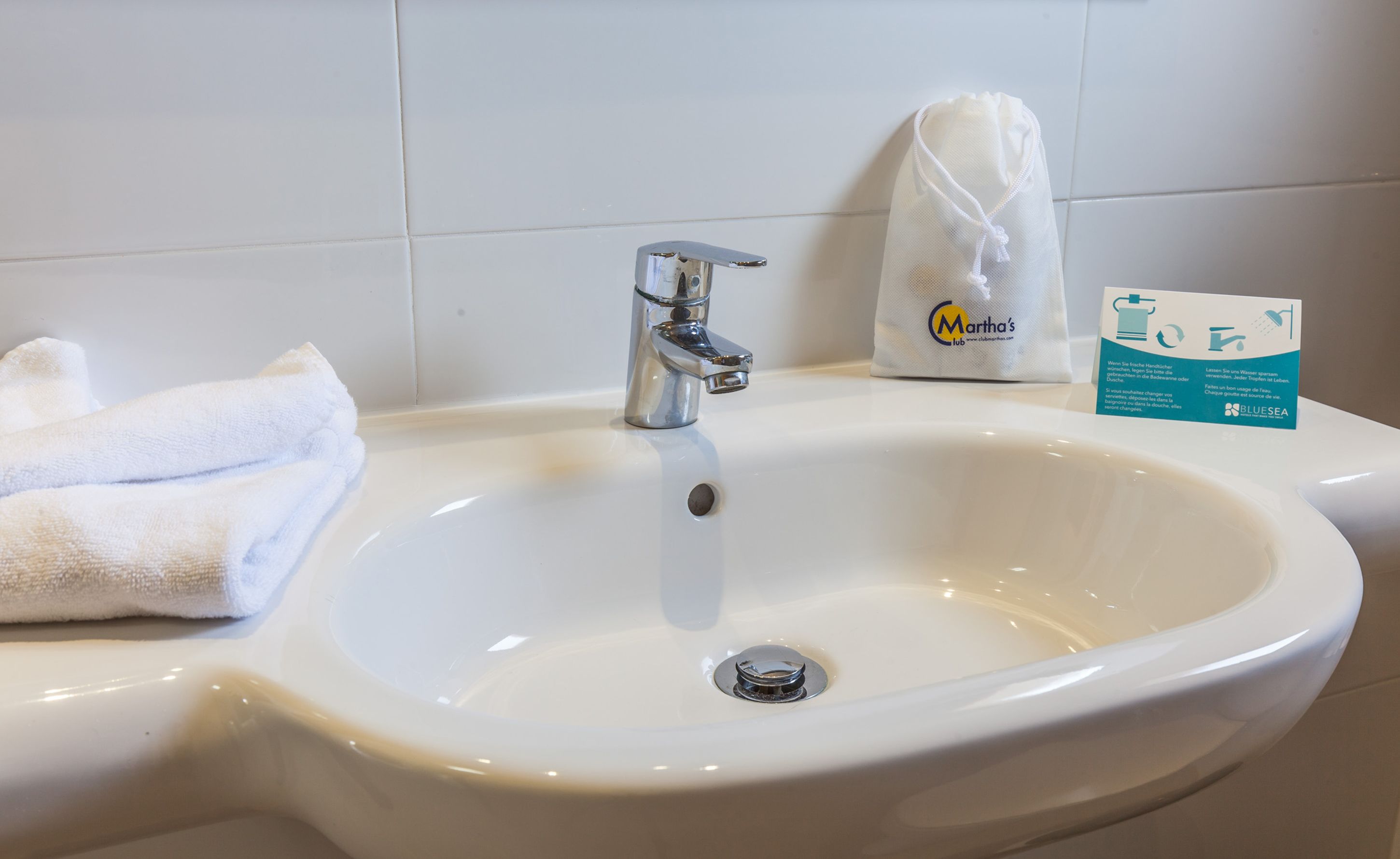 A white sink with a chrome faucet, a folded white towel, and a promotional sign for Martha's Lub.