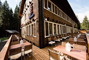 A wooden building with a restaurant patio featuring outdoor seating and a sign that reads "Johnson." - Eko sport hotel Björnson (Demanovska Dolina)