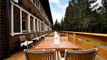 A wooden deck with a table and chairs, overlooking a forested area.