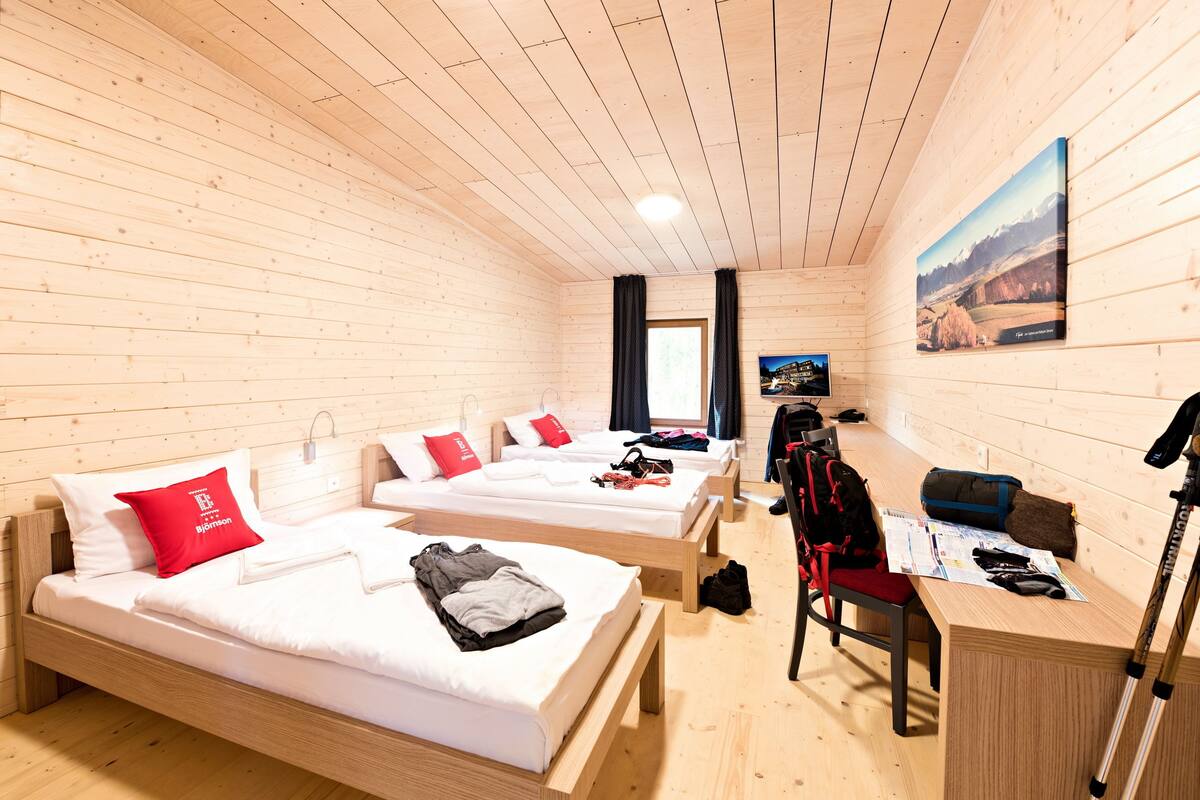 Una habitación tipo cabaña de madera con tres camas, un escritorio y una silla.