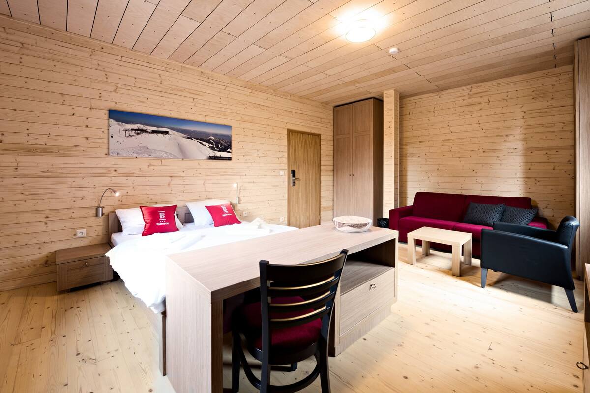 Un interior de madera con cama, escritorio, silla y sofá rojo.
