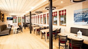 A restaurant with wooden floors, tables, and chairs, large windows with red curtains, and a mountain view painting on the wall. - Eko sport hotel Björnson (Demanovska Dolina)