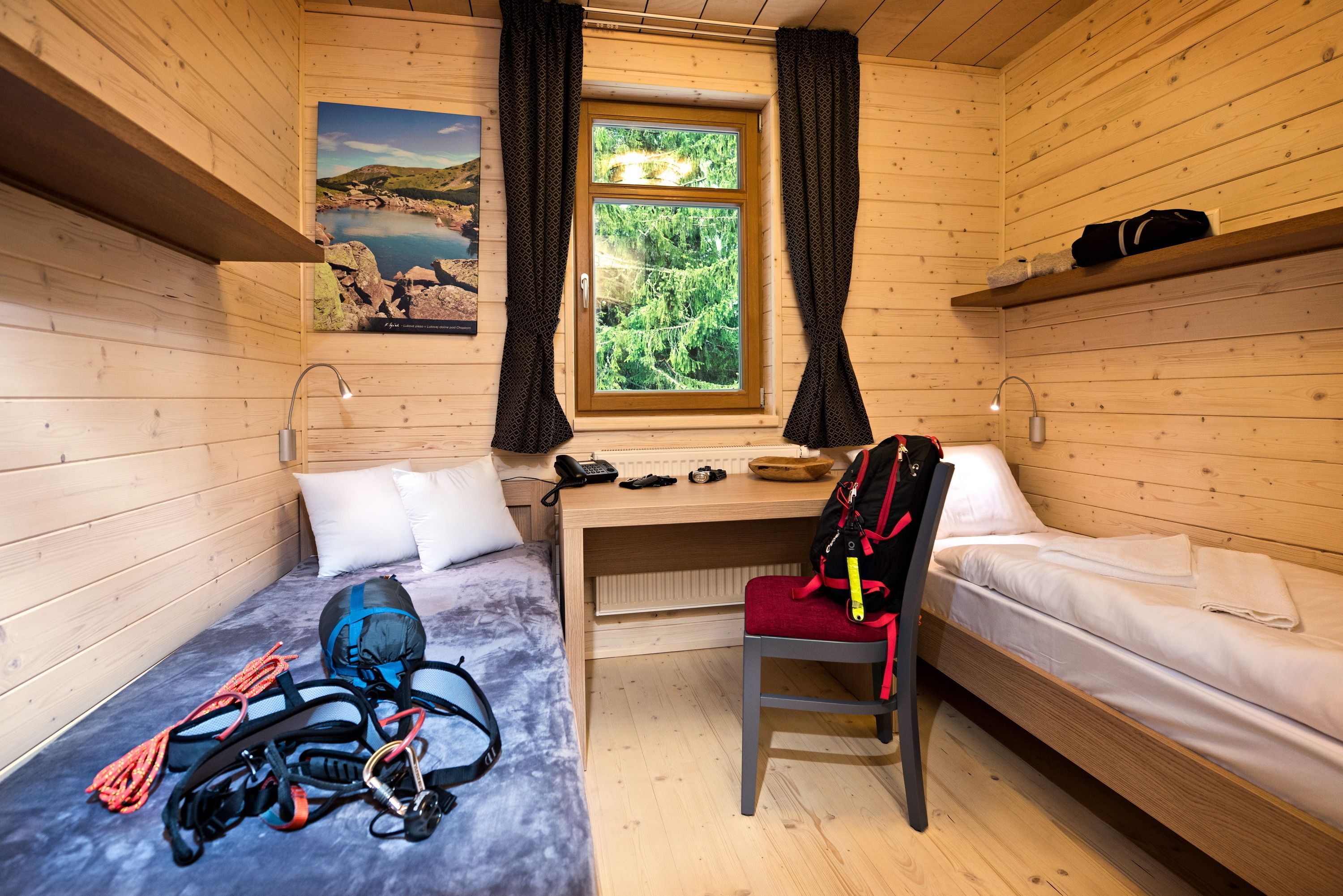 A cabin with two beds, a desk, a chair, and a window with a view of greenery.
