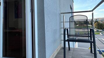 A balcony with a sliding glass door, a metal chair, and a view of a parking lot and distant landscape.