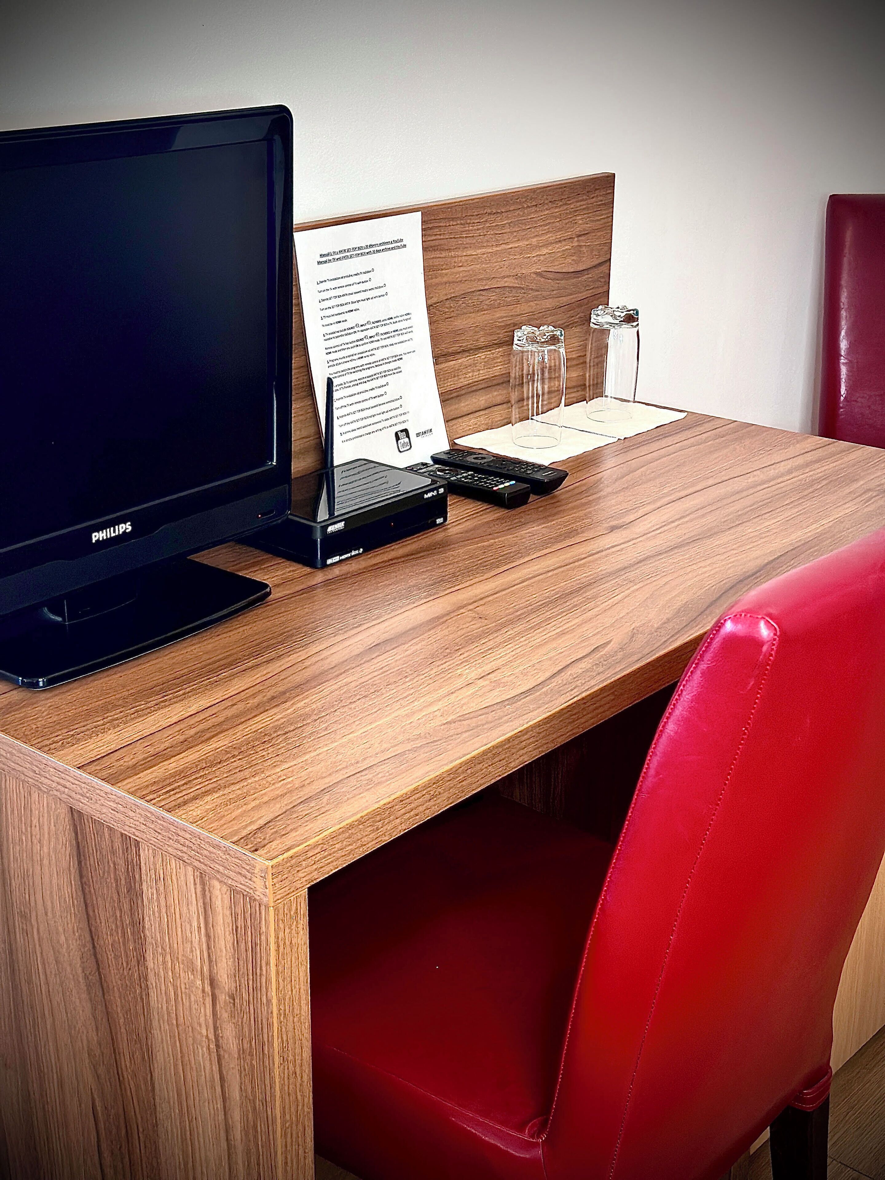 A wooden desk with a black monitor, a remote control, and a glass of water.
