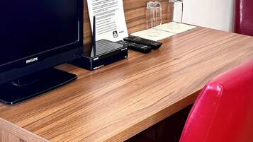 A wooden desk with a black monitor, a remote control, and a glass of water.