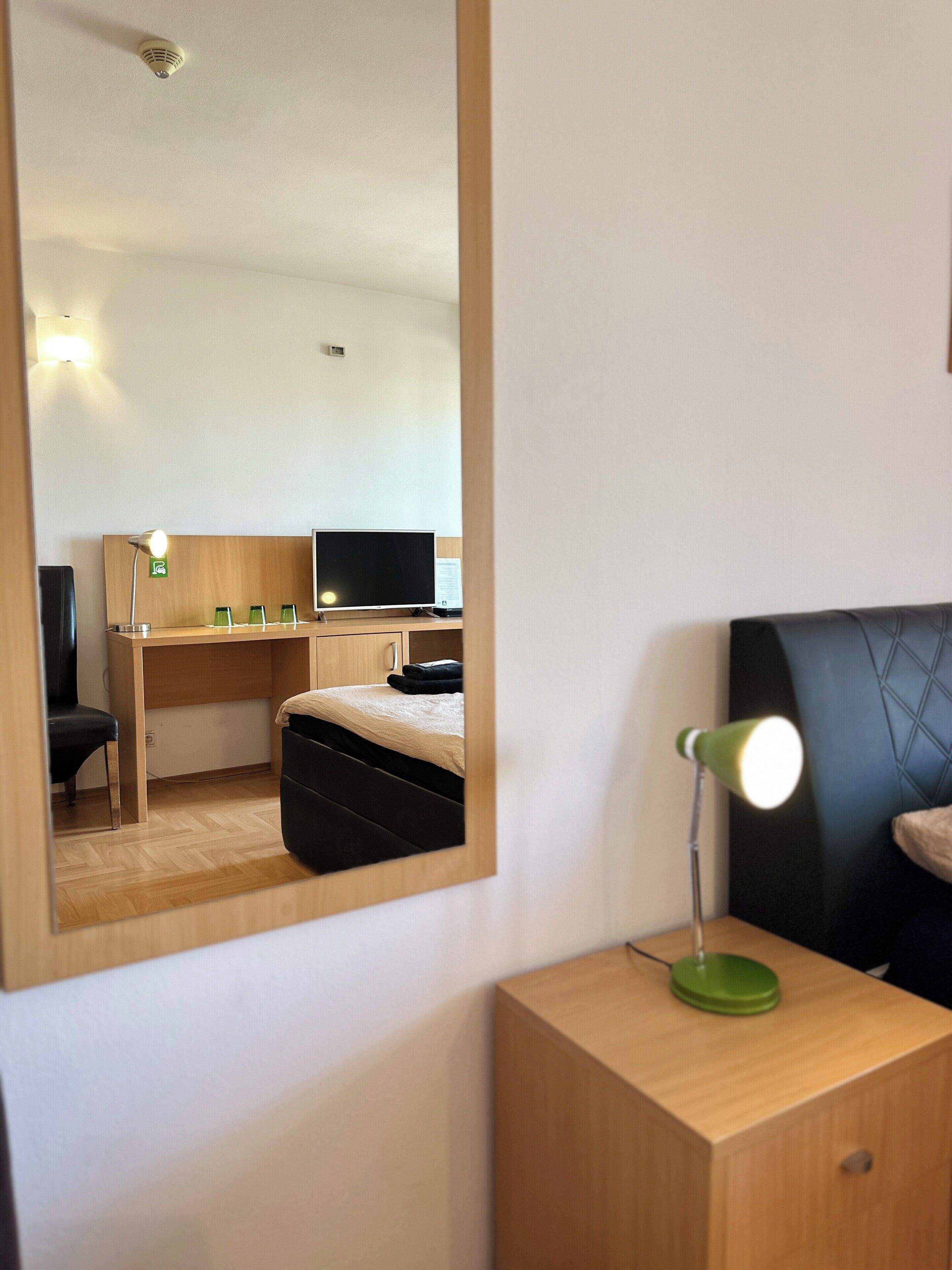 Habitación de hotel con un escritorio de madera, una cama, un televisor y una lámpara de escritorio verde.