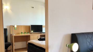 Habitación de hotel con un escritorio de madera, una cama, un televisor y una lámpara de escritorio verde.