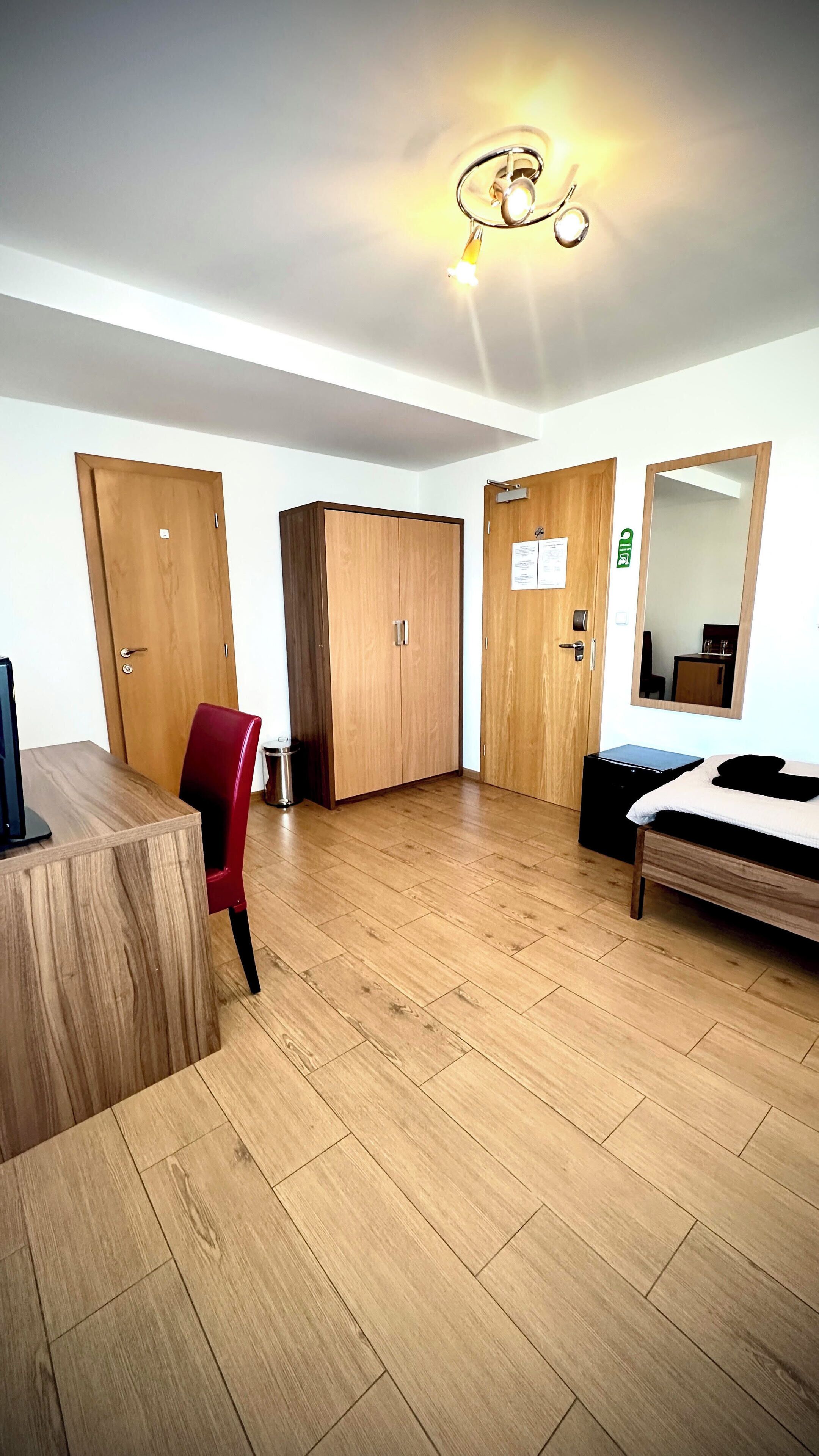 Habitación de hotel con piso de madera, un escritorio con silla, cama, armario y espejo.
