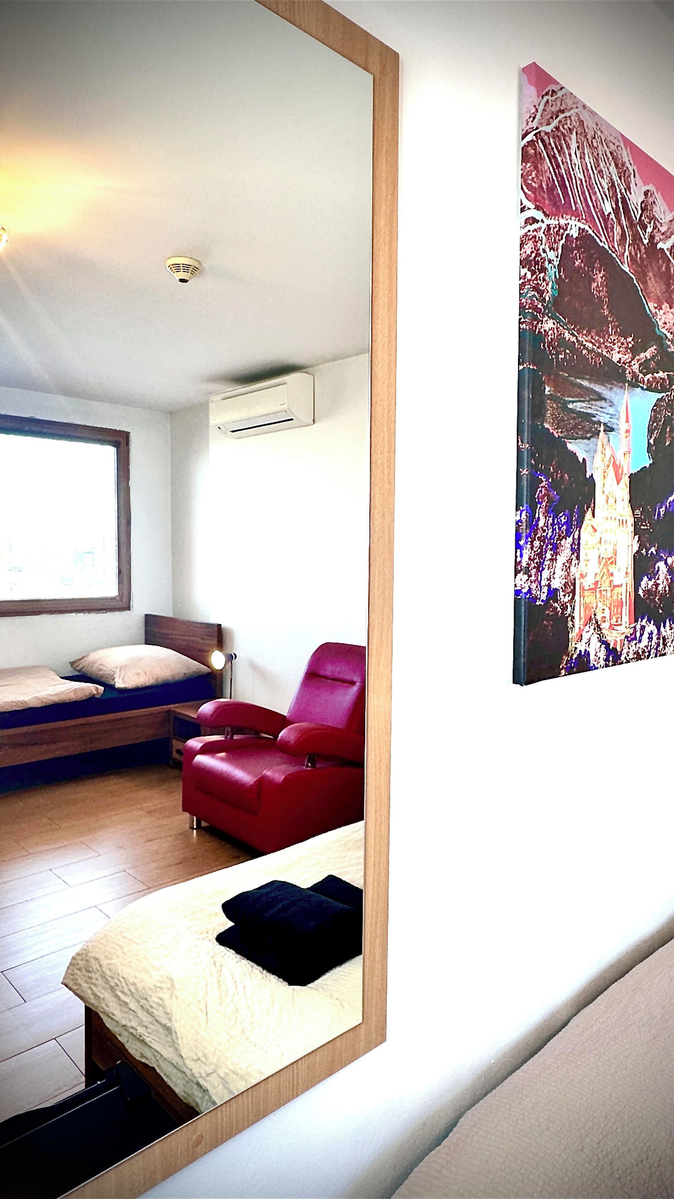 A bedroom with a bed, a red chair, a window, and a wall-mounted air conditioner.